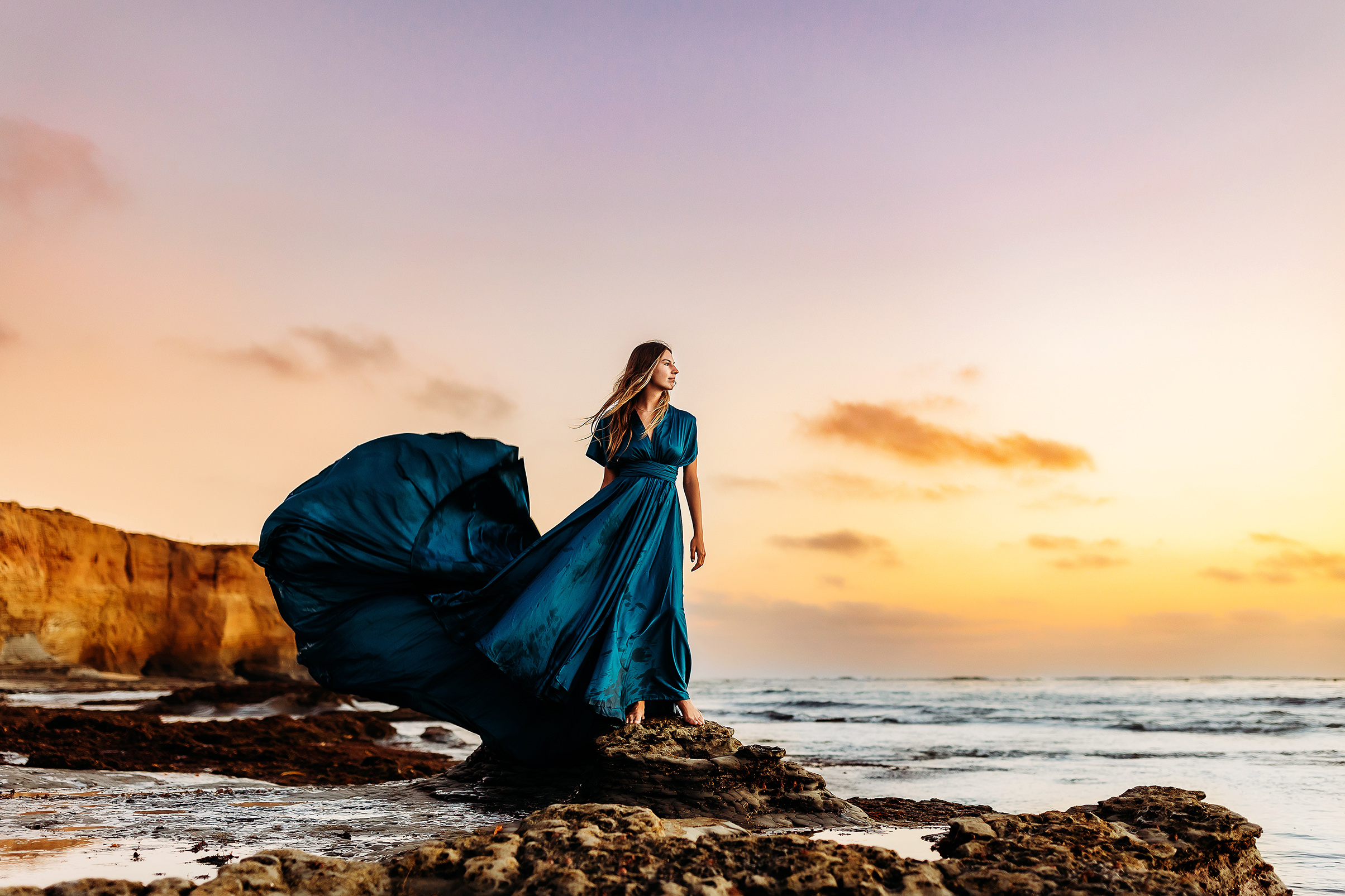 High school senior girl in a billowy dress looking out at the sunset.