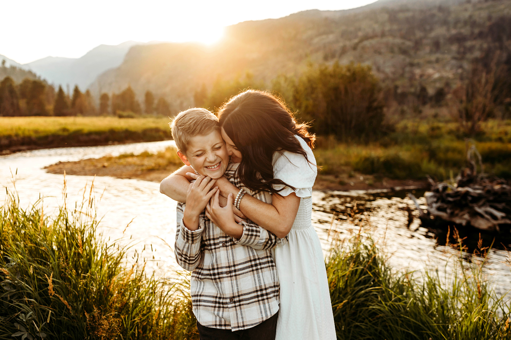 Mom hugging and kissing son at sunset in the Estes Park mountains.