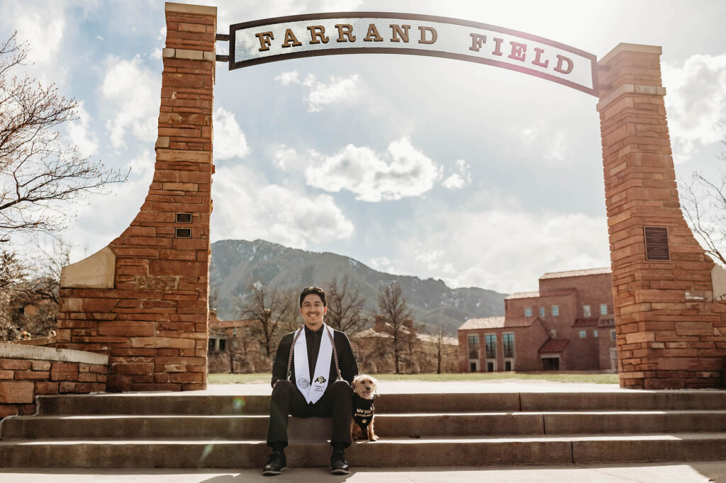 CU Boulder grad sitting on the steps of Farrand Field with his dog. 
