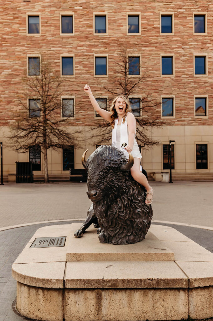 CU Boulder graduate celebrating with the Ralphie statue. 