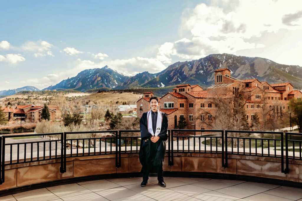 CU Boulder grad on the balcony of the Business building overlooking the Flatiron Mountains. 