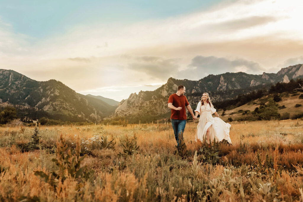 Husband and wife running through a field in the Boulder mountains at sunset. 