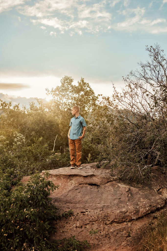 Little boy standing on a large boulder looking off into the sunset in Boulder, Colorado. 