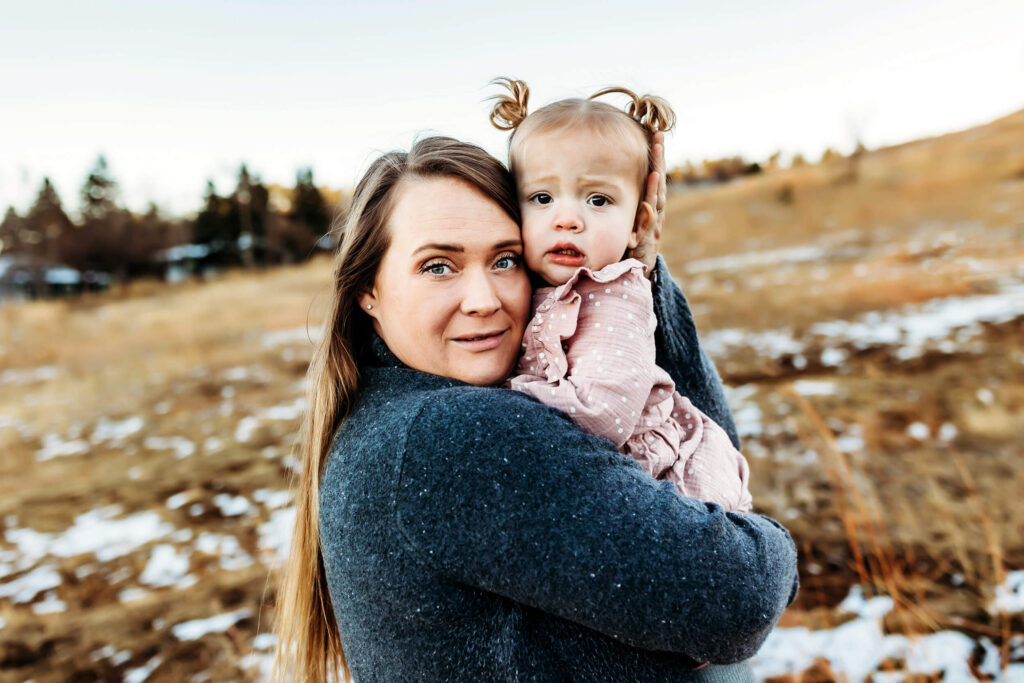 Mom holding toddler daughter and embracing in the cold winter Boulder air. 