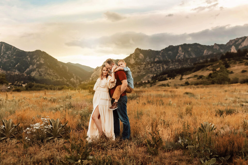 Mom, dad and son standing in a field in the mountains of Boulder. 