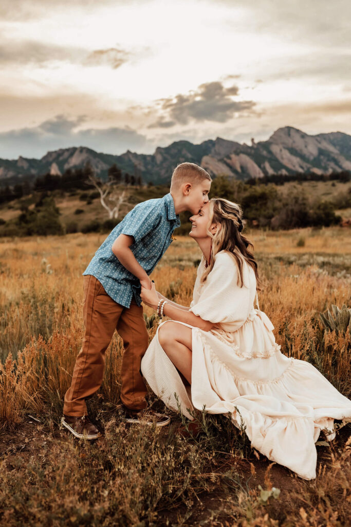 Son kissing his kneeling mom on the forehead in the Boulder sunset. 